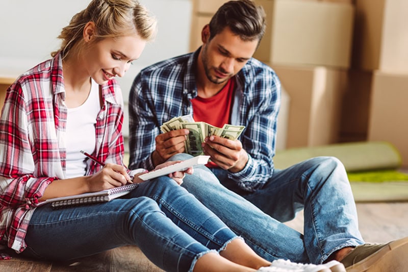 Think HVAC During Your Home Remodeling. Young couple counting money while sitting on floor in new apartment.