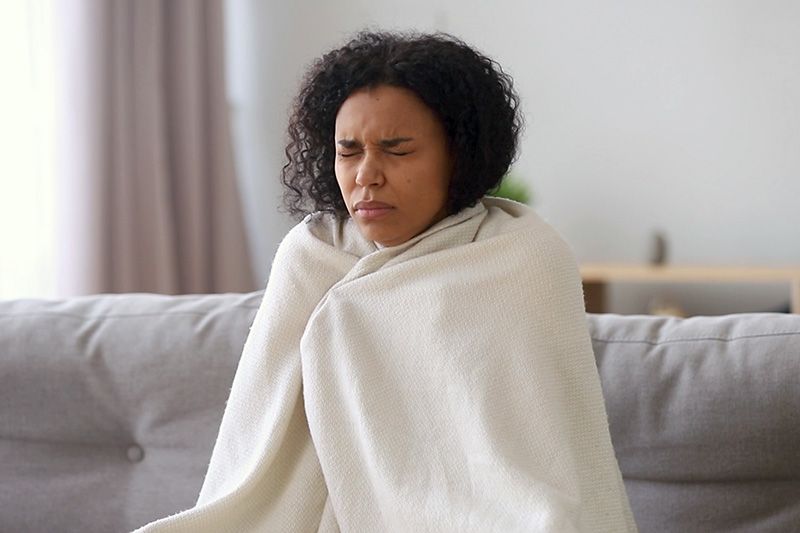 Video - Upgrade Your Furnace. Image shows woman sitting on couch and wrapped in a blanket.