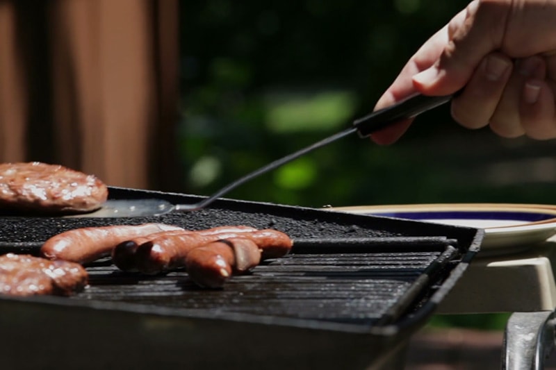A close up of a grill with hot dogs on it and a hamburger being flipped by a spatula.