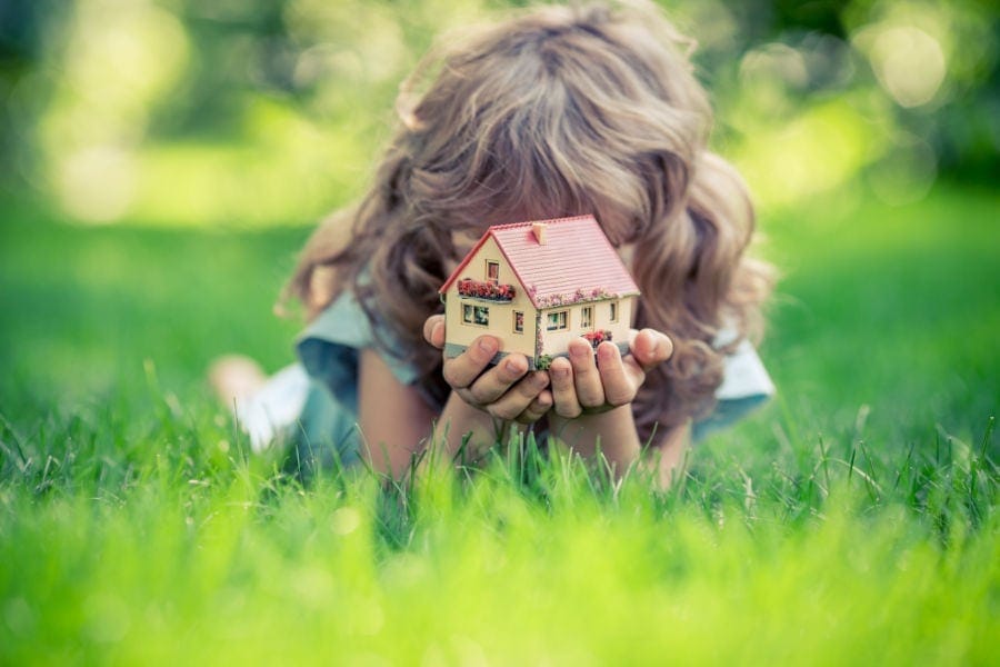 Young girl laying in the grass holding a little toy home.